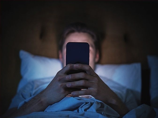 Person ligger i sängen och tittar på en mobiltelefon i mörkret